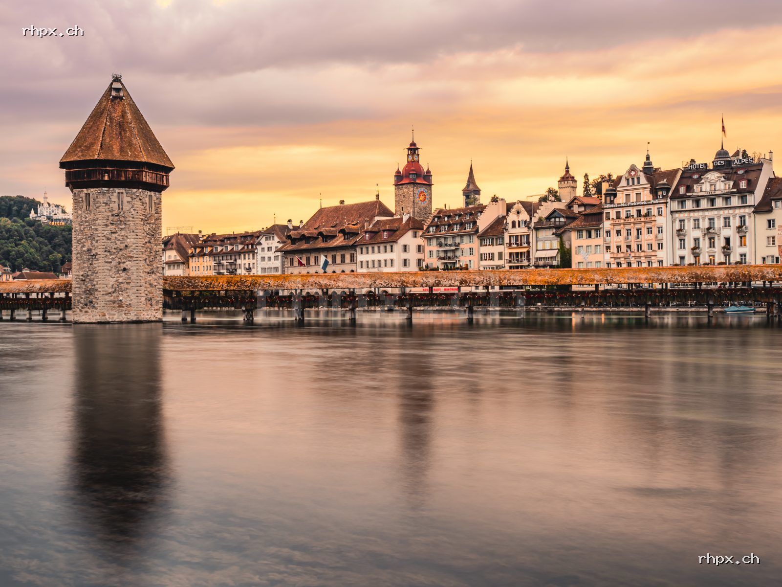 Chapel Bridge and Water Tower in Lucerne at sunset, calm Reuss river in the foreground, old town in the background