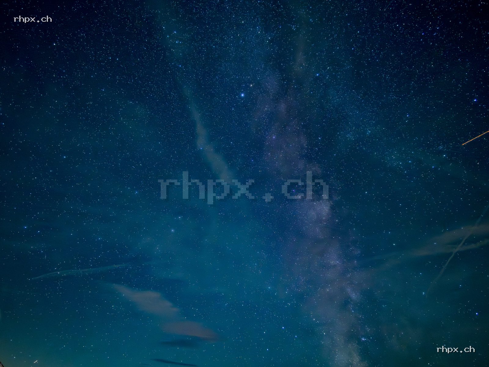 Milky Way centred in the frame against a deep blue starry sky, light cirrus clouds and an aircraft trail visible