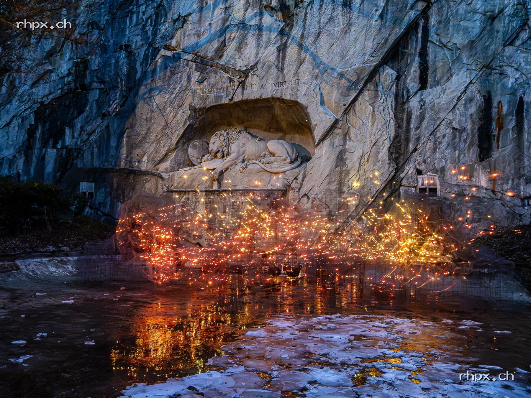 Lion Monument in Lucerne with colourful light installation, reflections in the water and rock wall in the background.