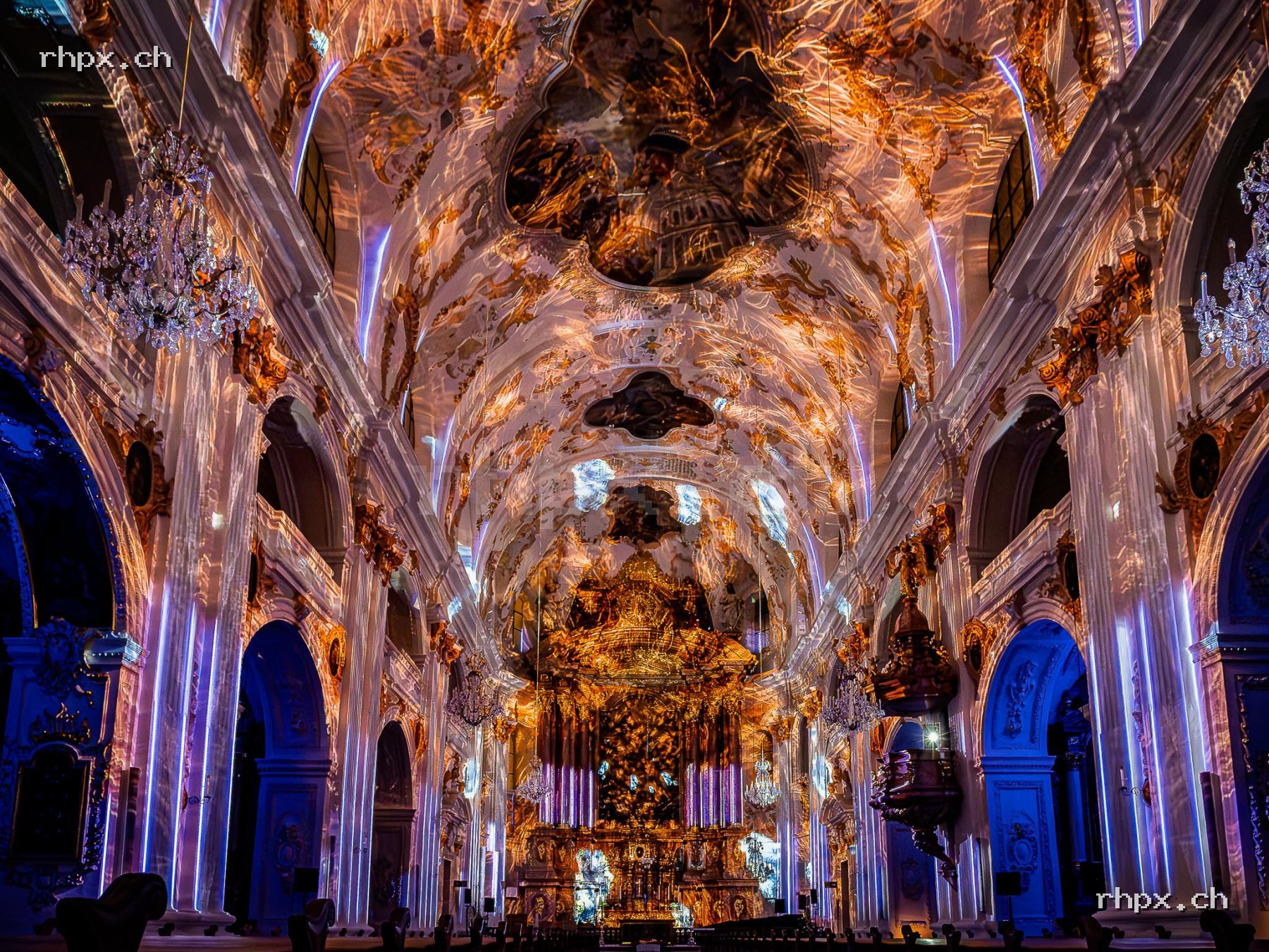 Baroque interior of the Jesuit Church in Lucerne with colourful light projections on ceiling, columns and altar.