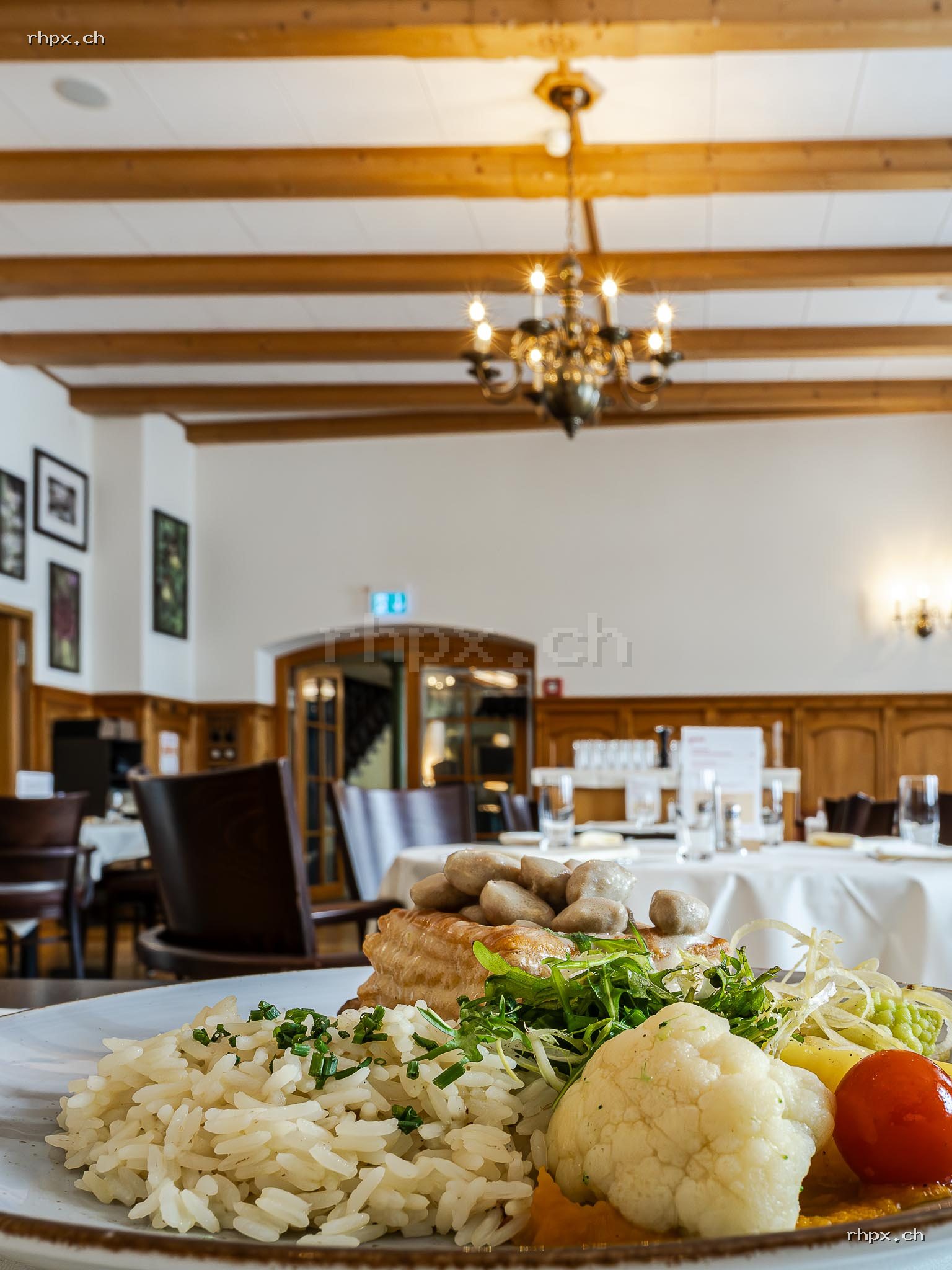 Pastetli dish with rice, vegetables and mushroom filling on a plate in a restaurant with set tables and wooden elements in the background.