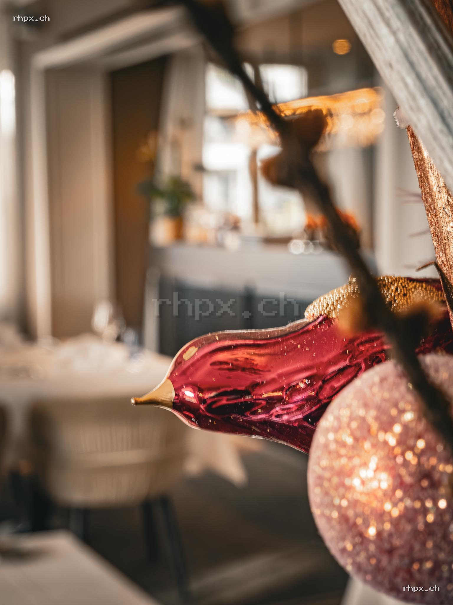 Red and pink Christmas ornament in the foreground with a softly blurred restaurant interior in the background.