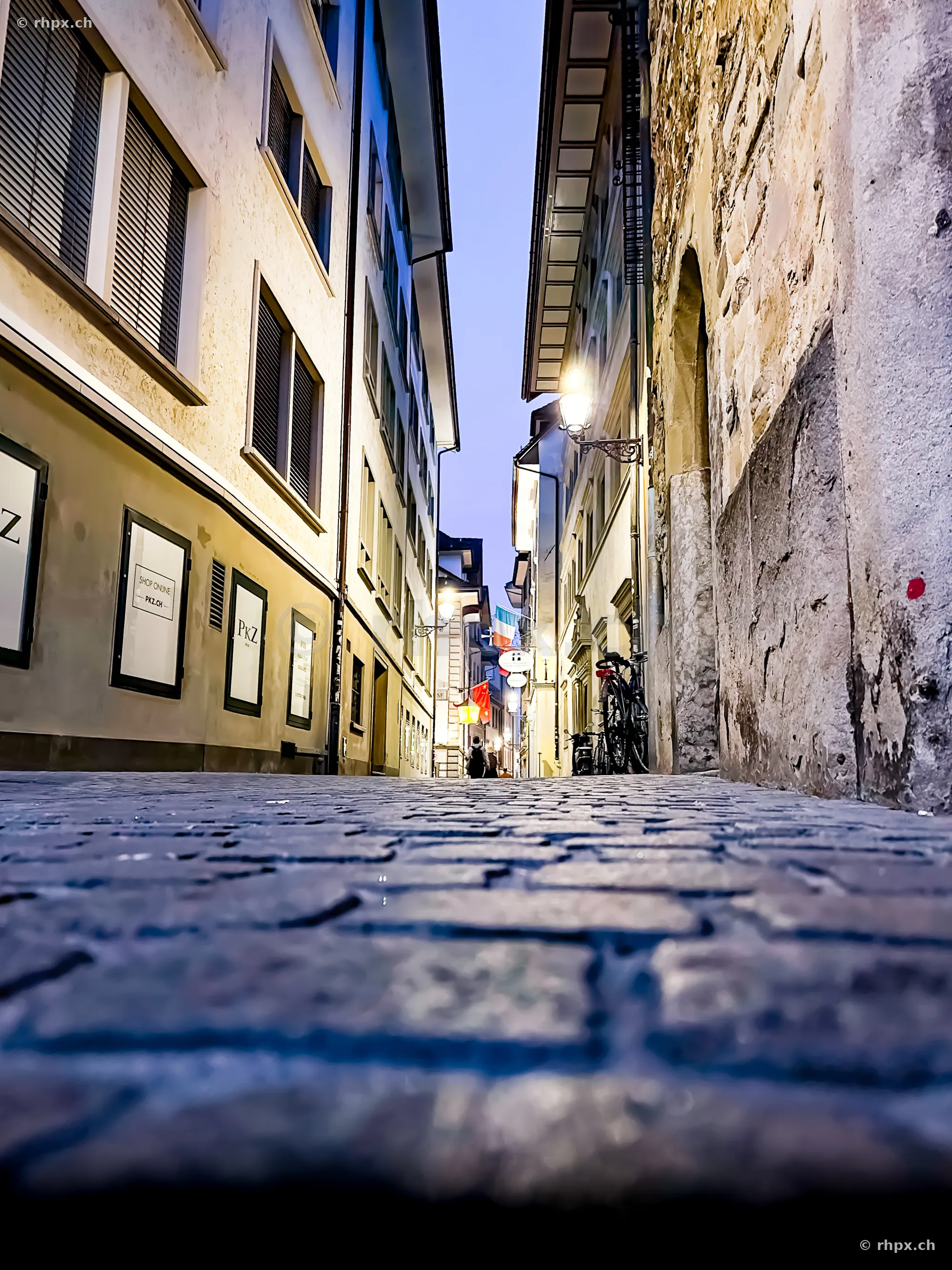 Tiefperspektive einer gepflasterten Gasse in der Altstadt von Luzern mit beleuchteten Hausfassaden.