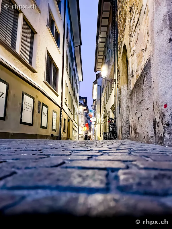 Tiefperspektive einer gepflasterten Gasse in der Altstadt von Luzern mit beleuchteten Hausfassaden.