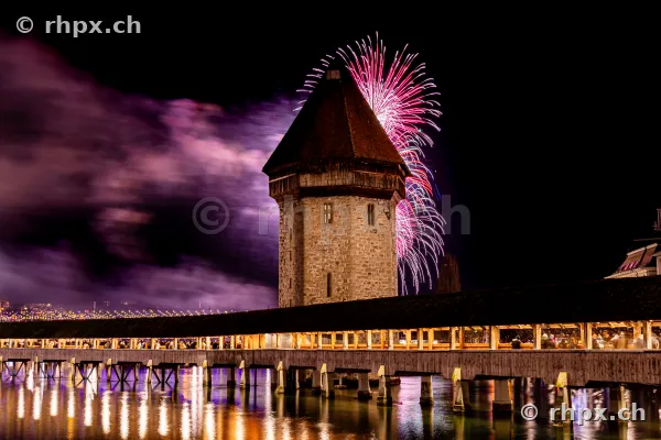 The illuminated water tower of the Chapel Bridge in Lucerne against New Year fireworks in 2024