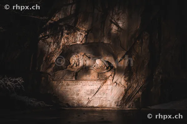 Das Löwendenkmal in Luzern beleuchtet bei Nacht vor einer Felswand