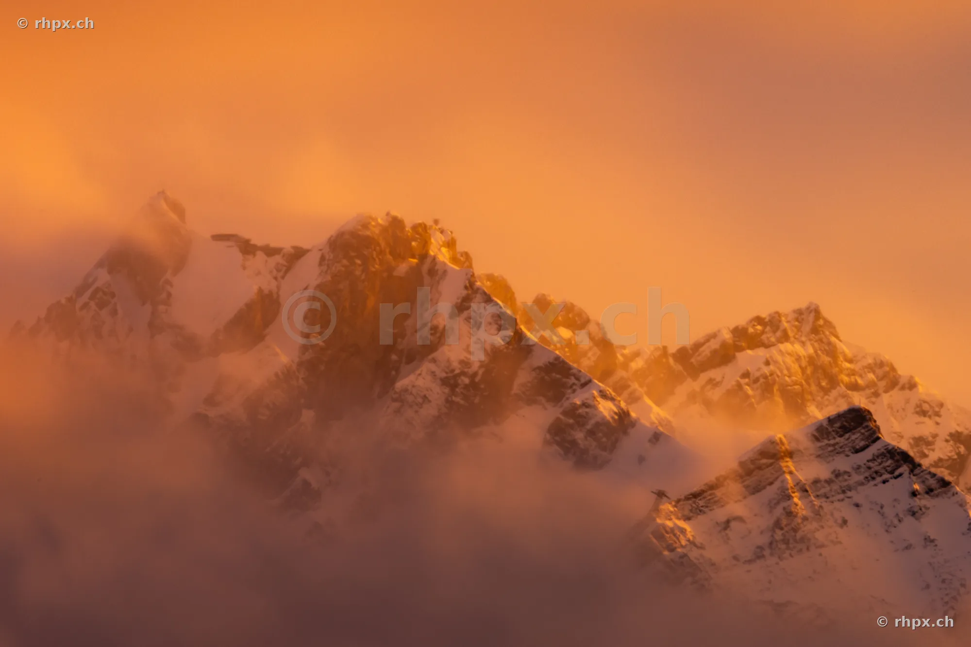 The snow-covered peak of Mount Pilatus in golden light surrounded by clouds