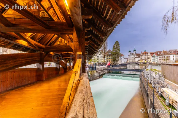 Blick aus dem hölzernen Innenraum der Spreuerbrücke in Luzern auf den Fluss Reuss und die Altstadt.