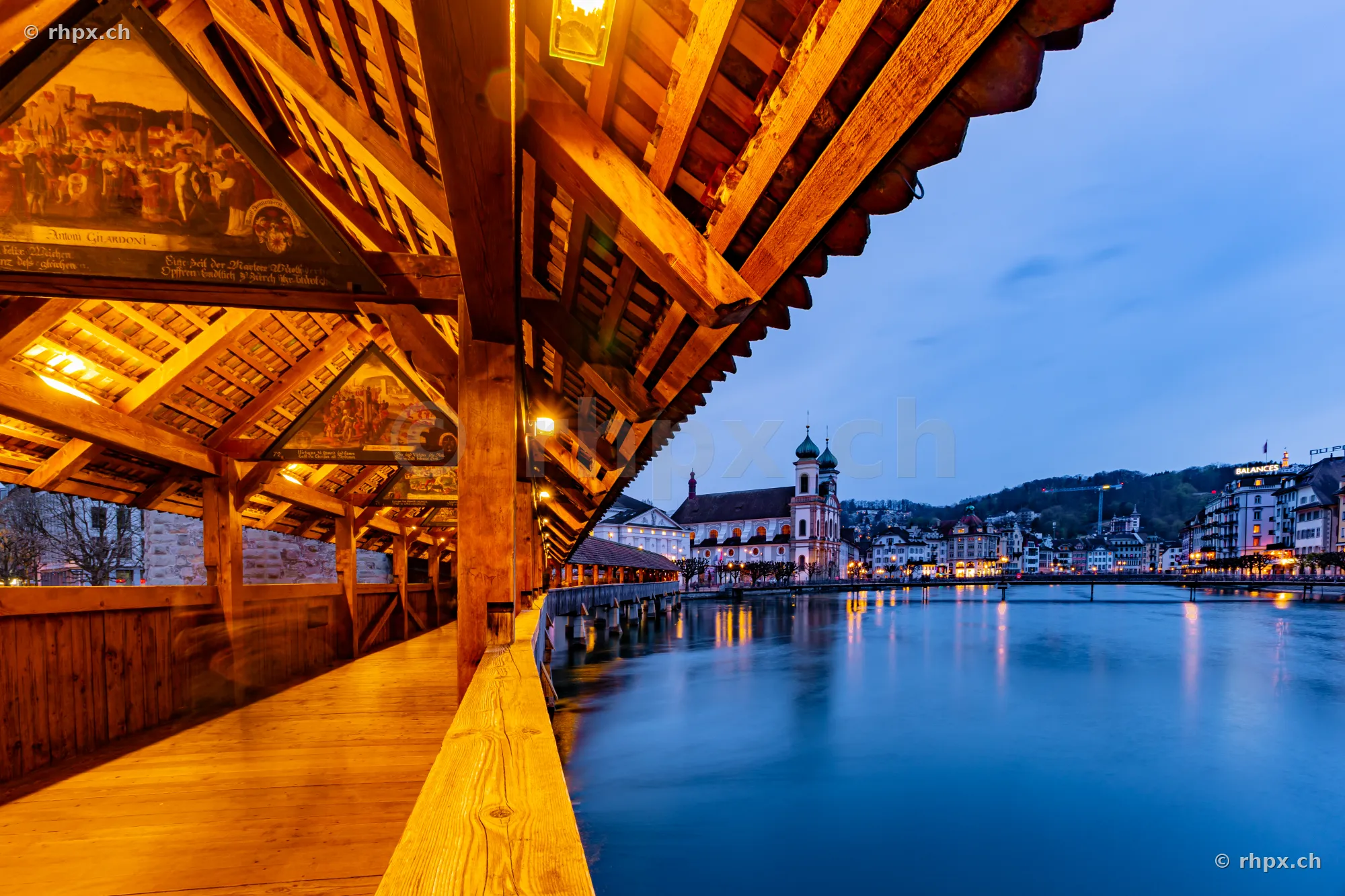 View from the wooden Chapel Bridge in Lucerne towards the Jesuit Church and the Reuss river during the blue hour
