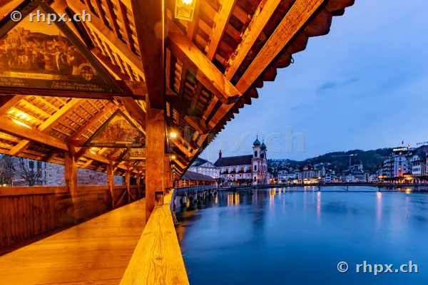 Blick aus der hölzernen Kapellbrücke in Luzern auf die Jesuitenkirche und den Fluss Reuss während der blauen Stunde