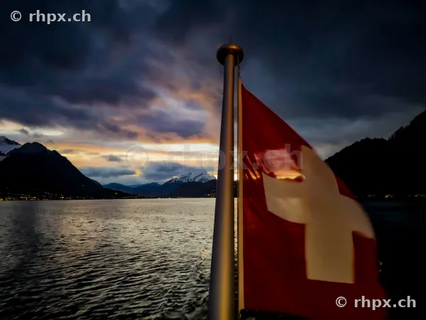 Schweizer Fahne am Heck eines Schiffes auf dem Vierwaldstättersee mit Bergen im Hintergrund