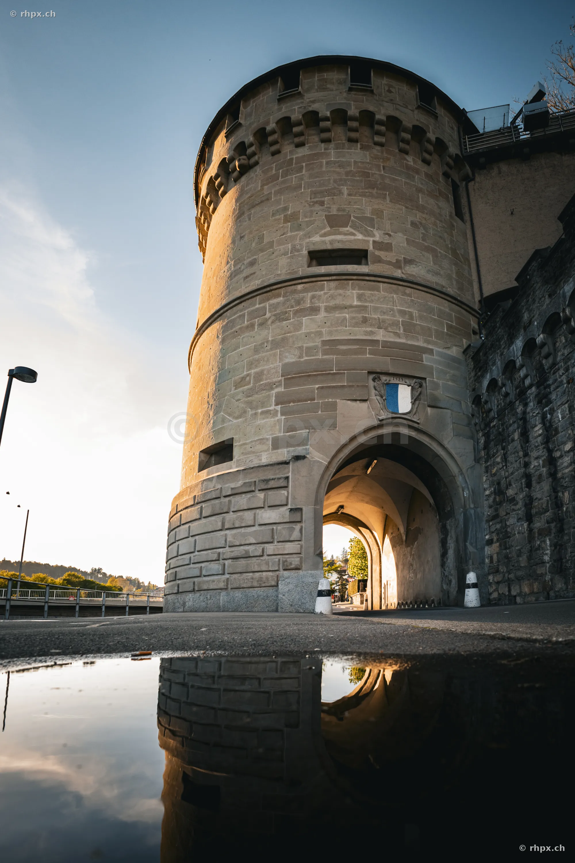The Zytturm with archway in Lucerne in evening light reflected in a puddle.