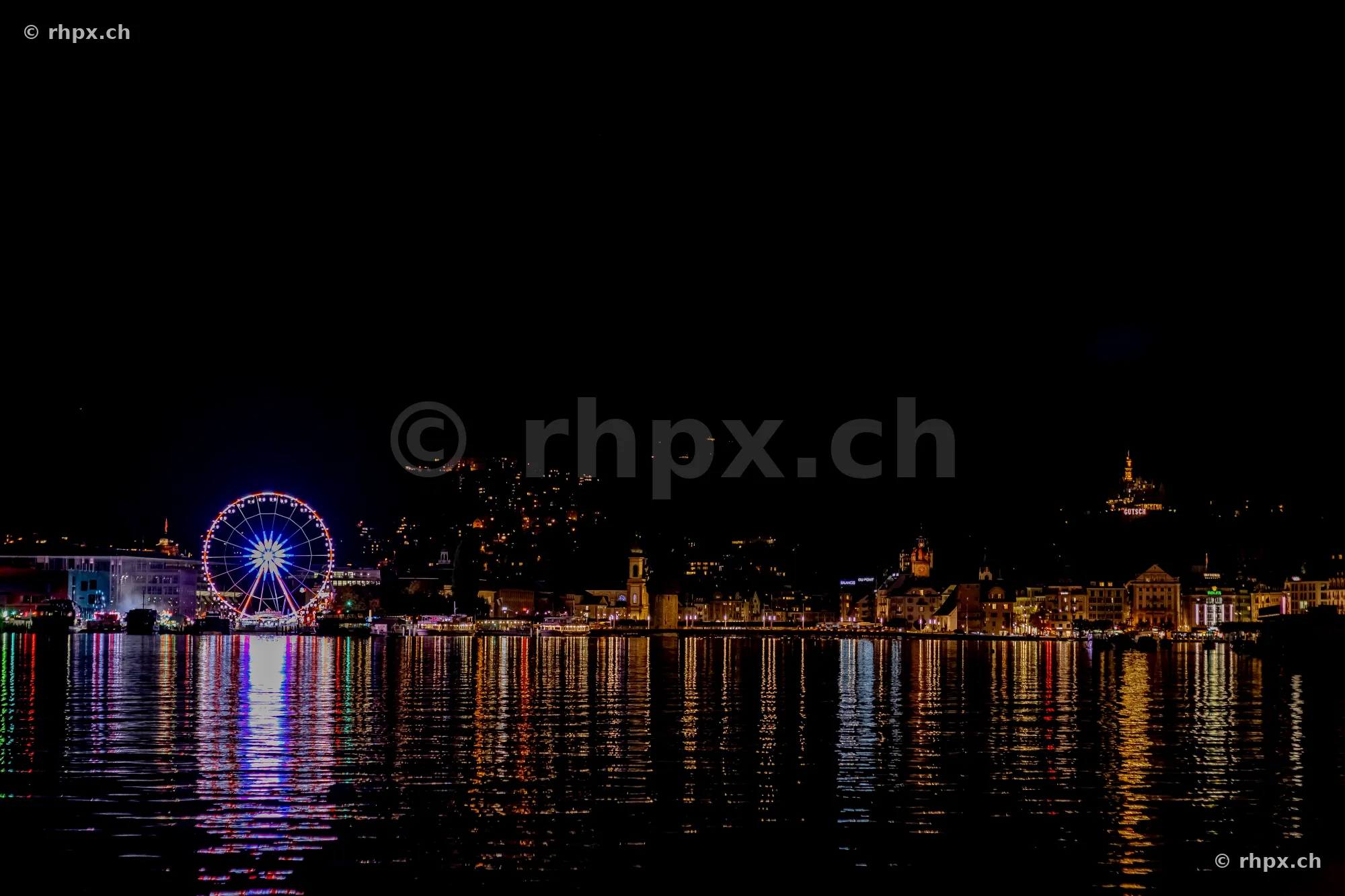 Night view of the illuminated Ferris wheel and the city skyline of Lucerne by Lake Lucerne