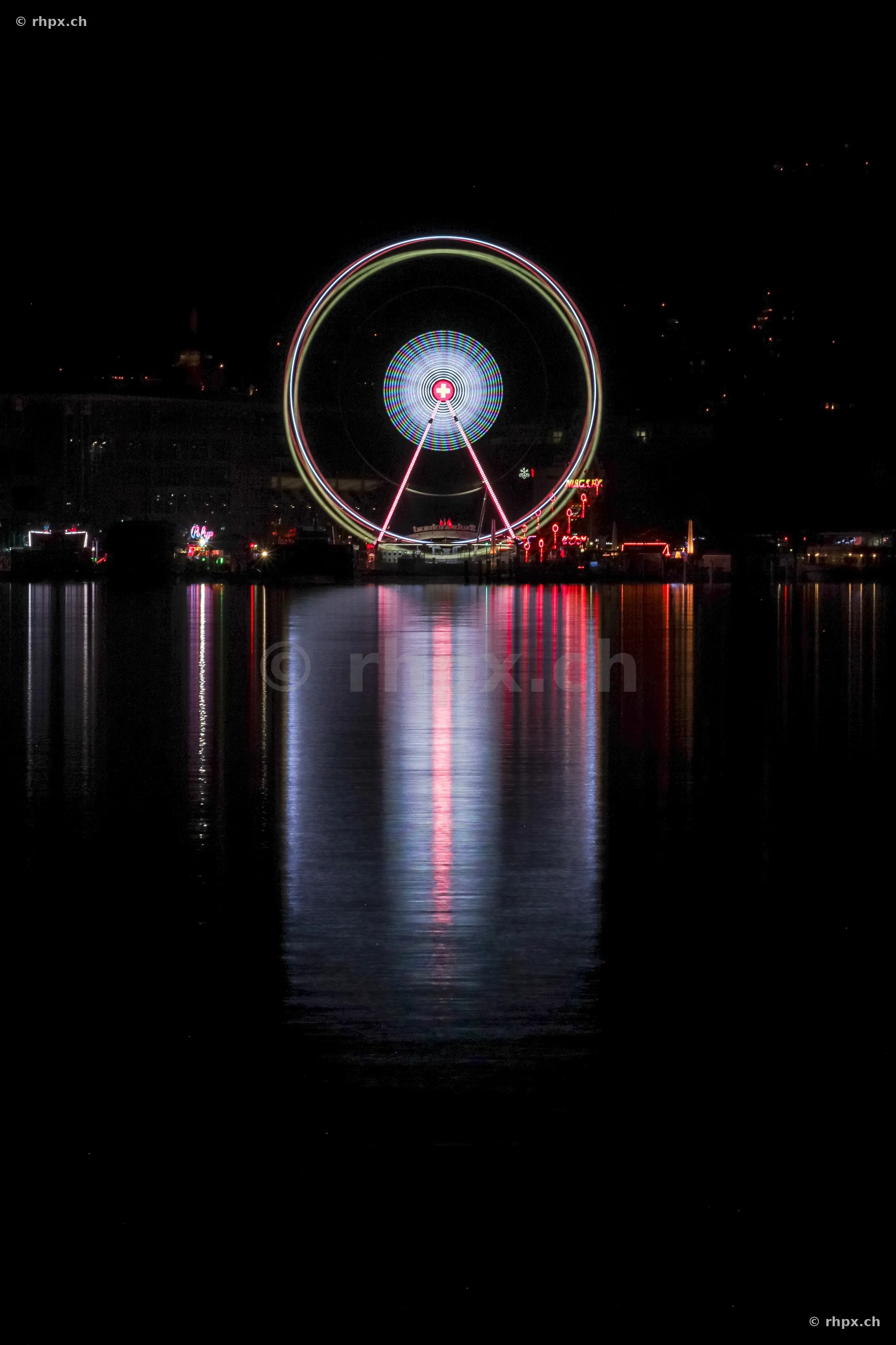 Illuminated Ferris wheel on the shore of Lake Lucerne at night with reflections in the water