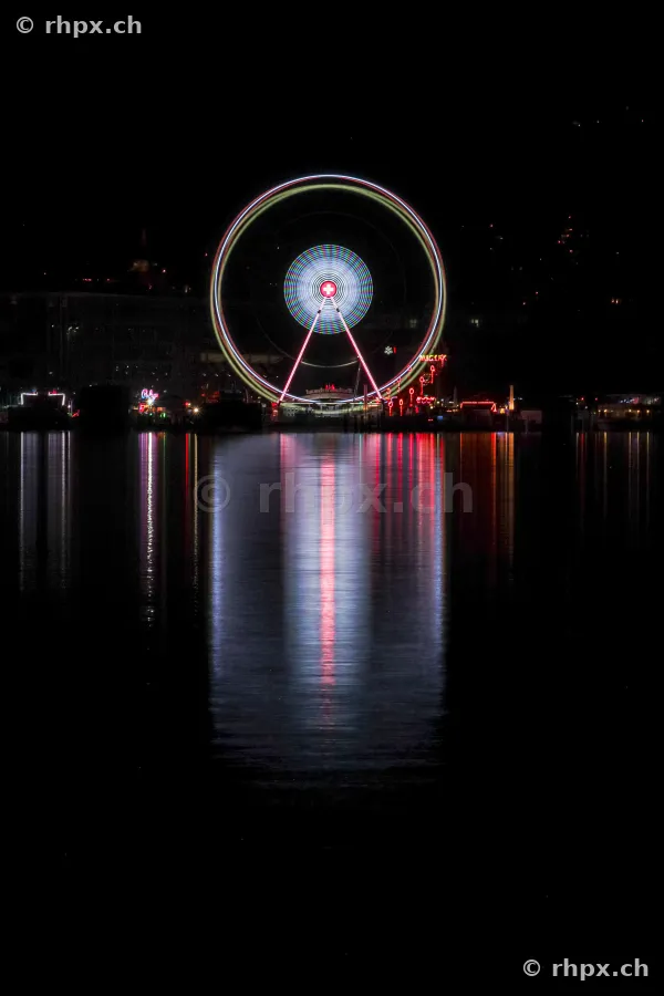 Beleuchtetes Riesenrad am Ufer des Vierwaldstättersees in Luzern bei Nacht mit Spiegelung im Wasser