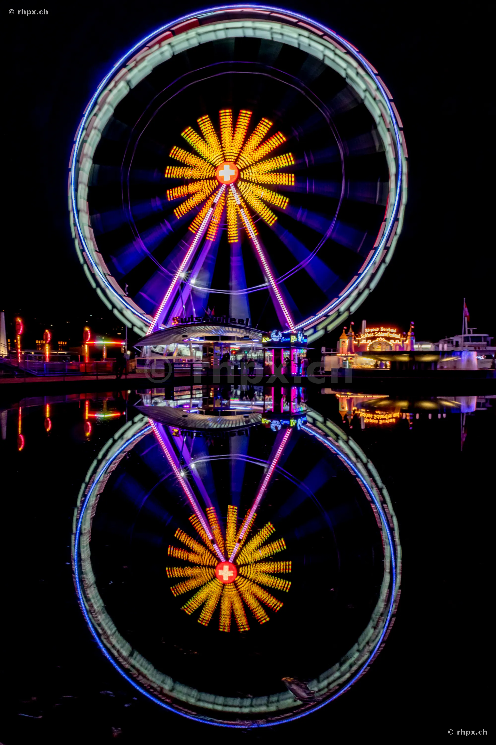 Illuminated Ferris wheel reflecting in the dark water of Lake Lucerne.