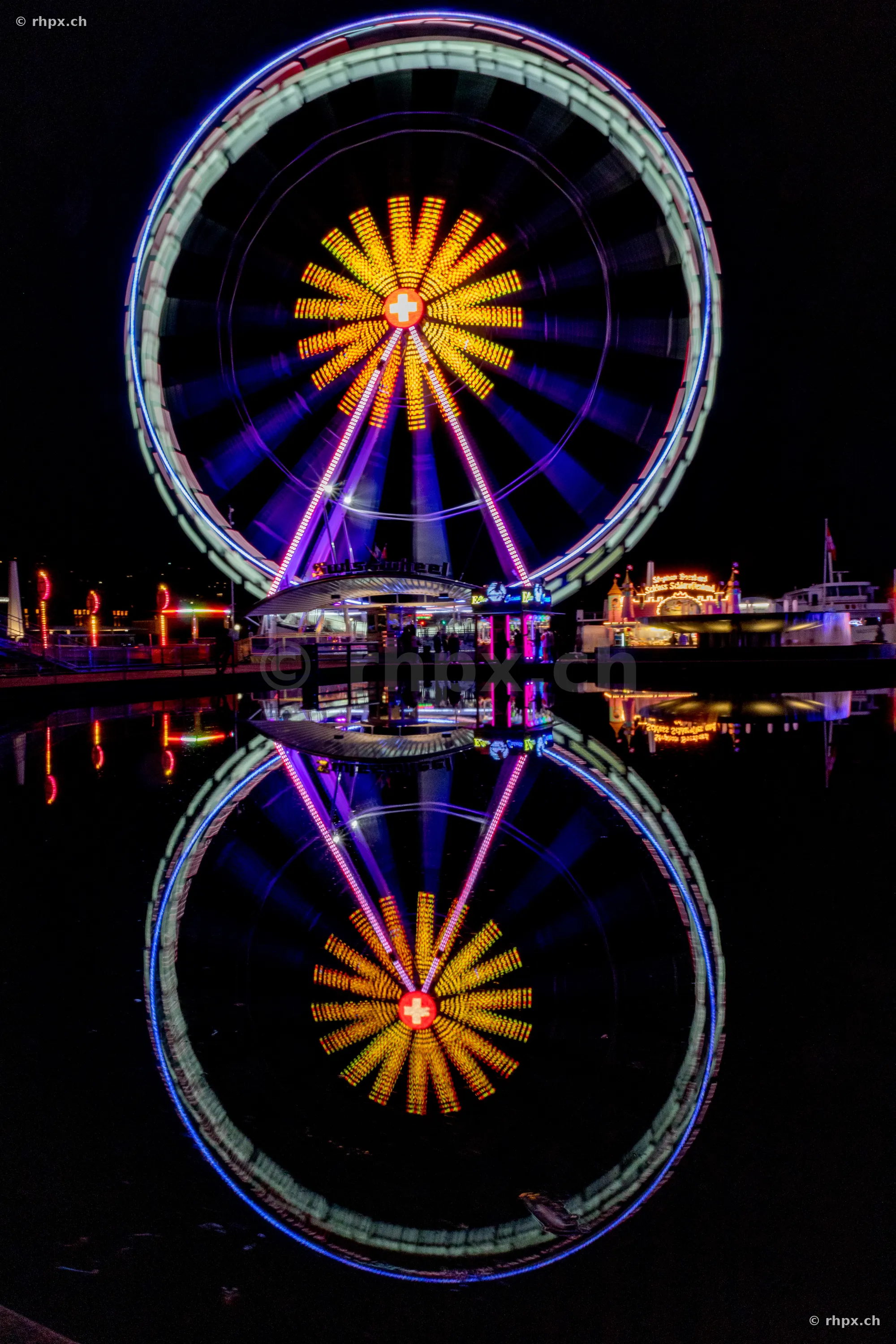 Illuminated Ferris wheel at the lake basin in Lucerne at night with reflection in the water