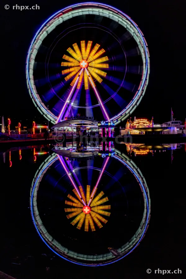 Beleuchtetes Riesenrad am Luzerner Seebecken bei Nacht mit Reflexion im Wasser