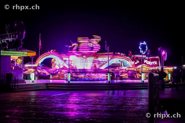 Beleuchtetes Fahrgeschäft mit Lichtspuren auf einem nächtlichen Jahrmarkt