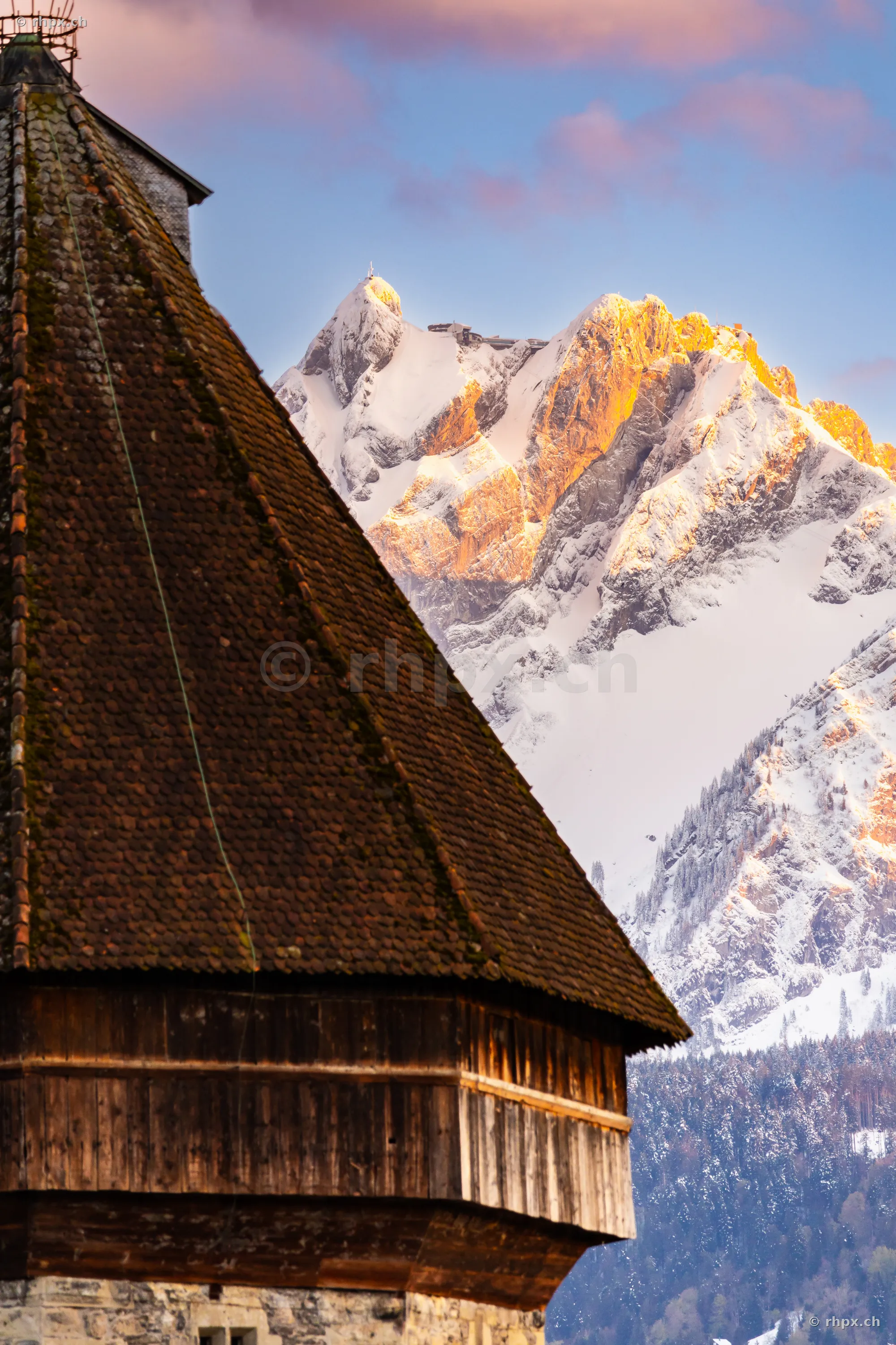The sloped roof of the Water Tower in Lucerne with the snowy peak of Mount Pilatus in the background during daylight.