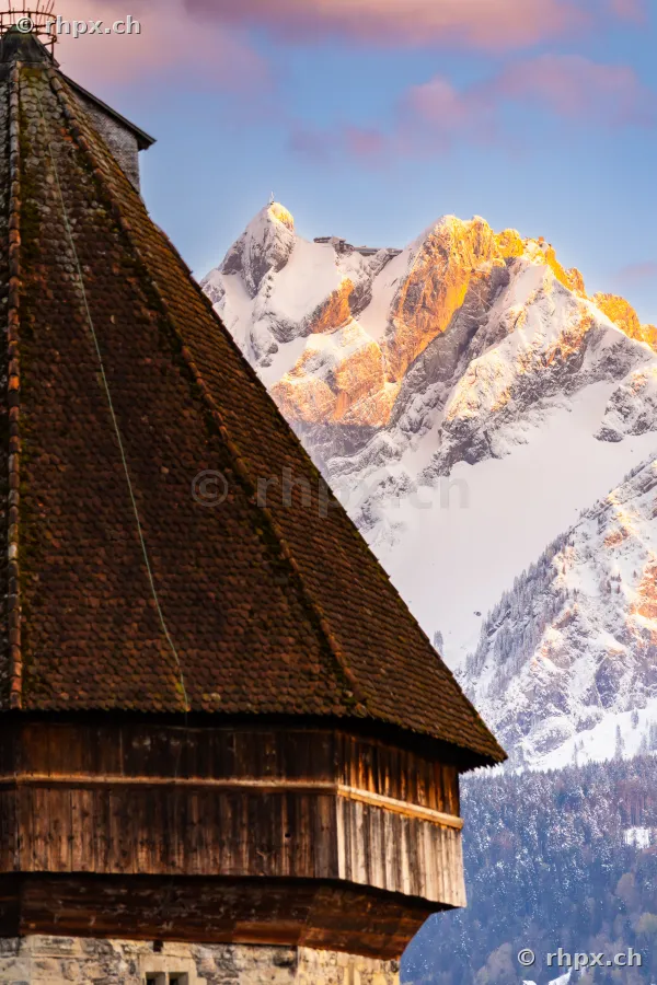 Das schräge Dach des Wasserturms in Luzern mit dem verschneiten Gipfel des Pilatus im Hintergrund bei Sonnenlicht.