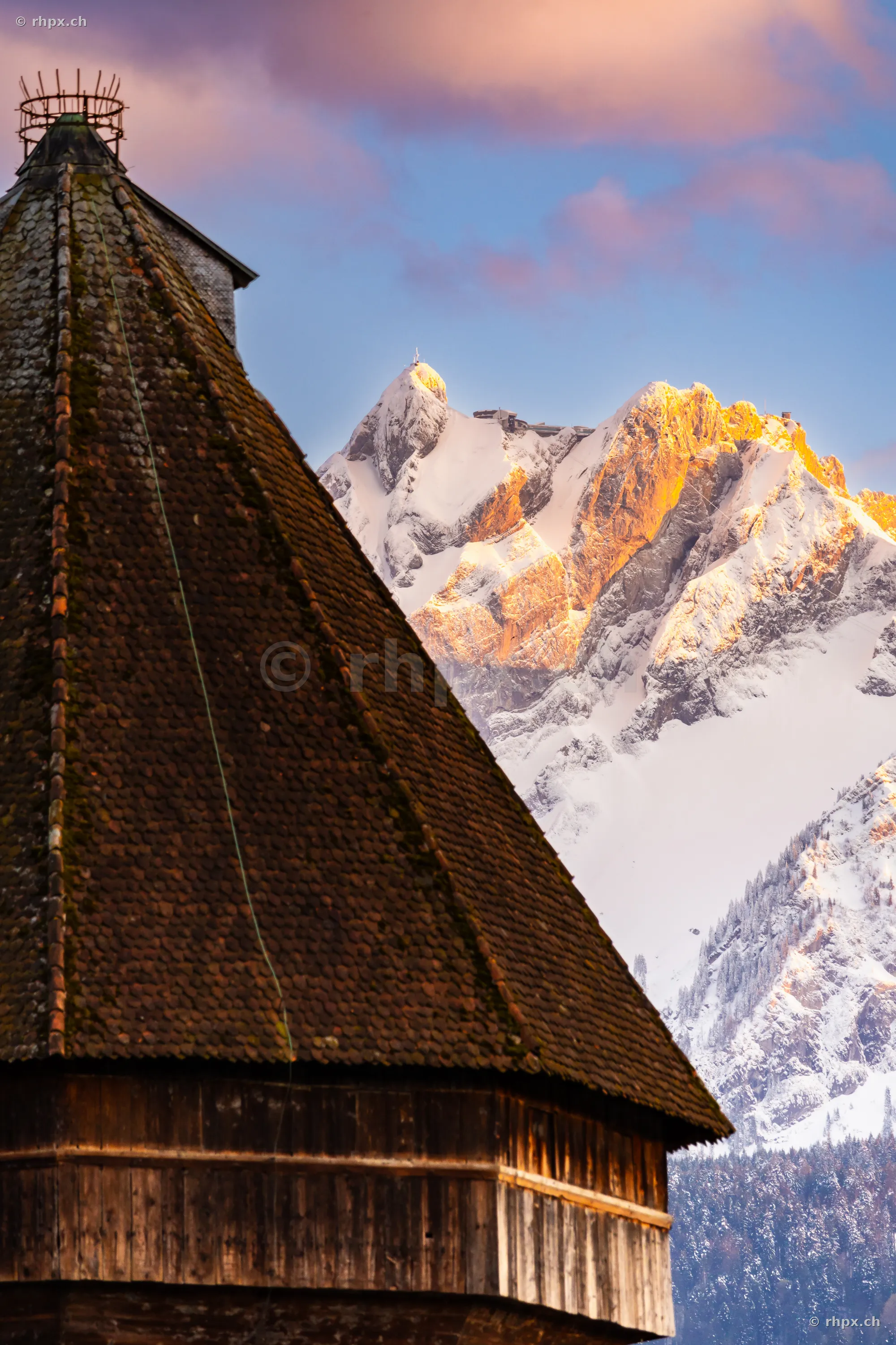 Close-up of a tower roof in Lucerne with the snow-covered Mount Pilatus in the background during evening light
