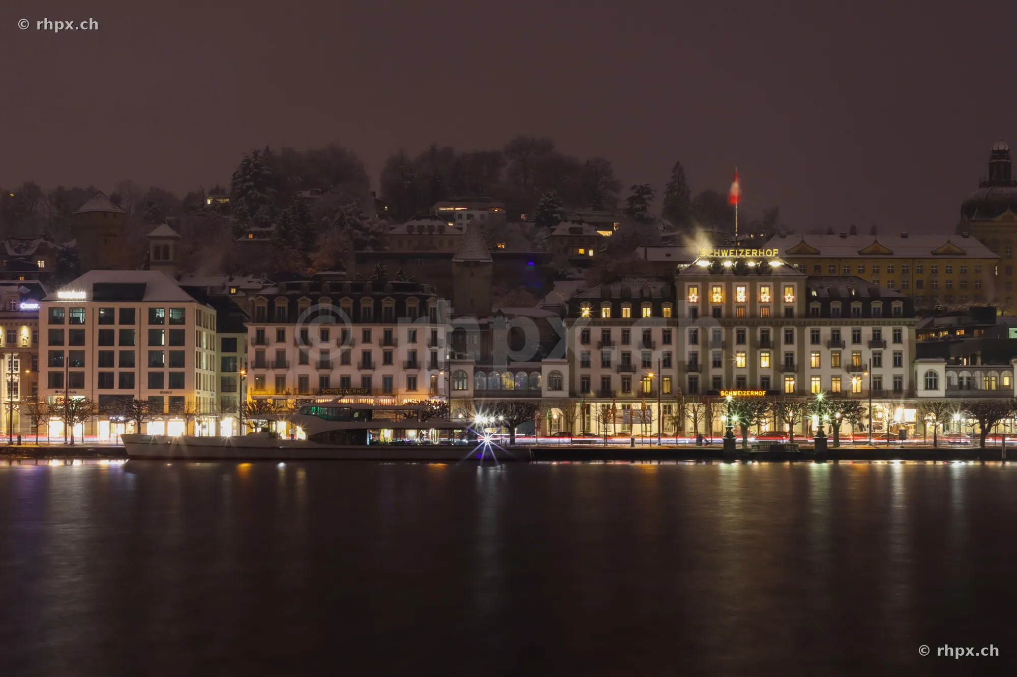 Illuminated buildings along the Lake Lucerne shore in Lucerne at night with light snow