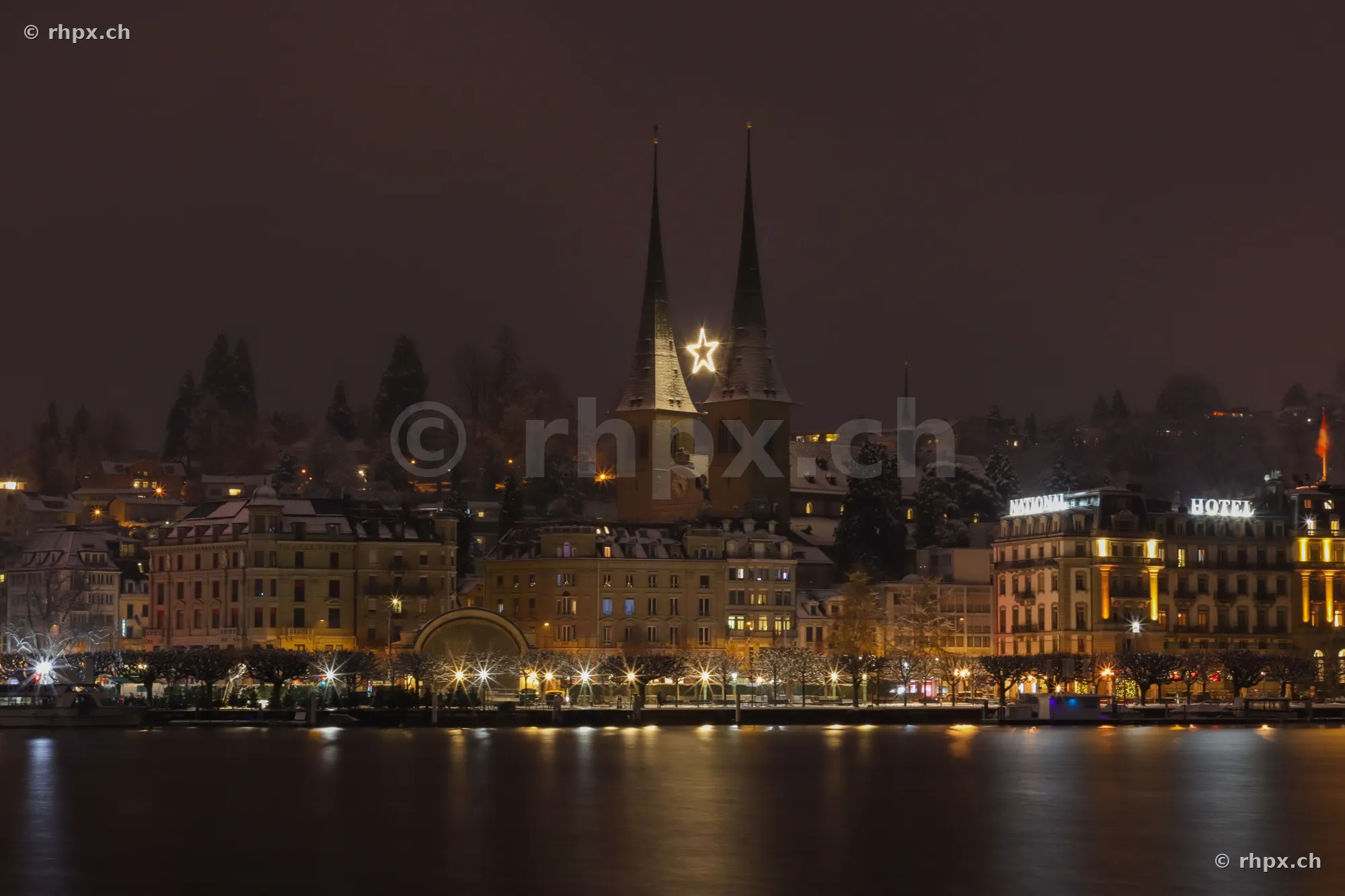 View of the Hofkirche in Lucerne at night with an illuminated Christmas star between the towers.