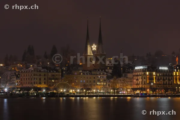 Blick auf die Hofkirche in Luzern mit beleuchtetem Weihnachtsstern zwischen den Türmen bei Nacht.