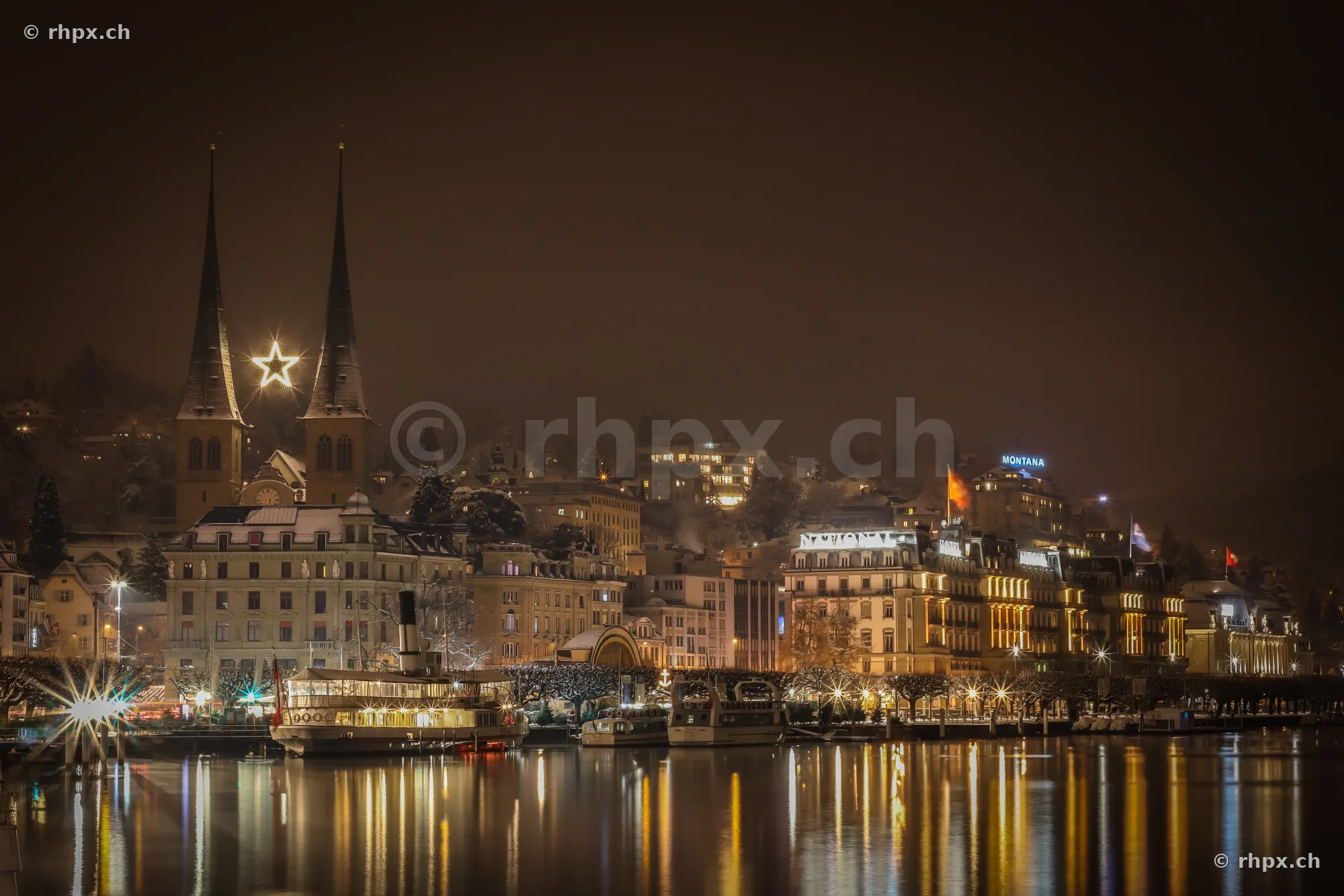 Hofkirche and lakeside promenade in Lucerne at night with an illuminated ship in the foreground