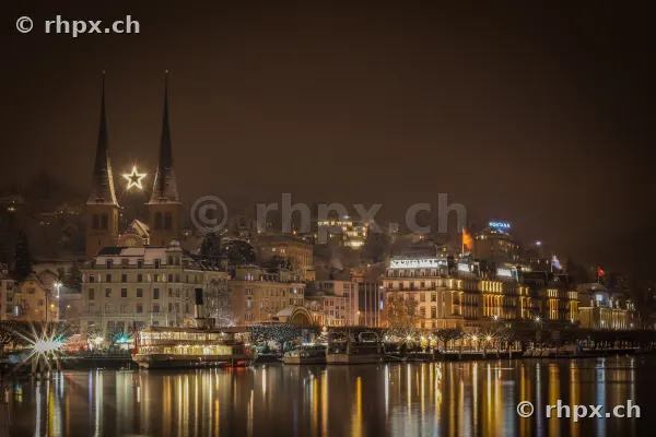 Hofkirche und Uferpromenade in Luzern bei Nacht mit einem beleuchteten Schiff vor der Kulisse