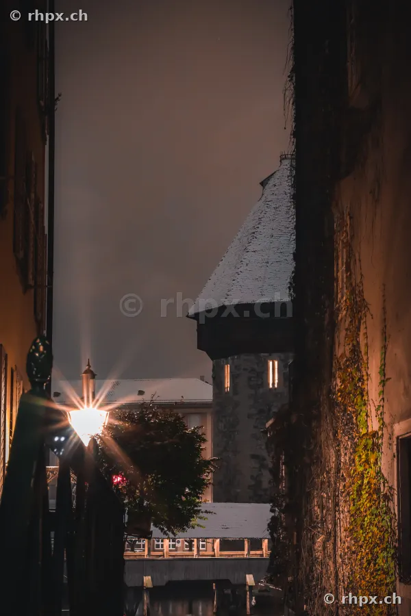 Der Wasserturm in Luzern bei Nacht, gerahmt von Gassenfassaden und einer Strassenlaterne.