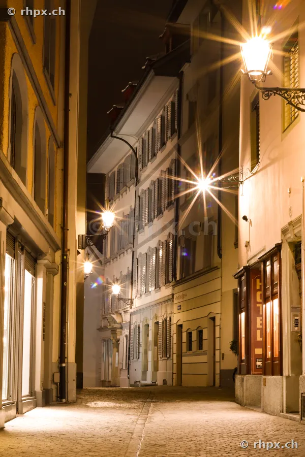 Nachtaufnahme einer engen gepflasterten Gasse in der Luzerner Altstadt mit beleuchteten Strassenlaternen