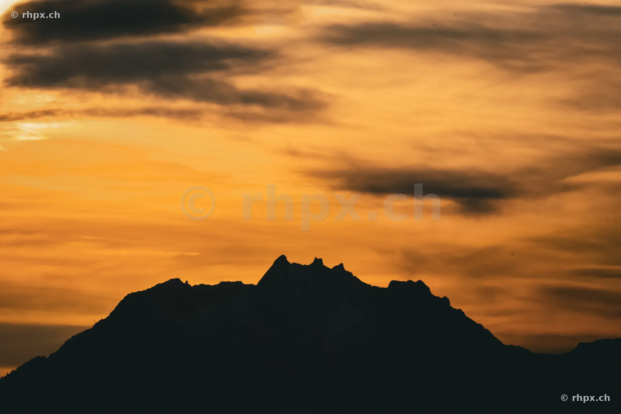 Dunkle Silhouette des Berges Pilatus vor einem orange gefärbten Abendhimmel