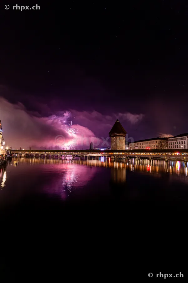 Fireworks in the night sky above the illuminated Chapel Bridge and Water Tower in Lucerne