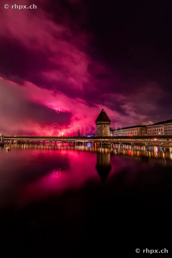 Nächtliche Ansicht der beleuchteten Kapellbrücke in Luzern während eines violetten Feuerwerks