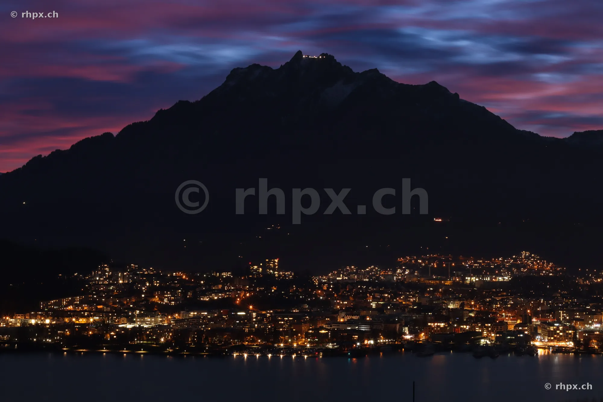 Silhouettes of Mount Pilatus against a purple evening sky above the illuminated city of Lucerne