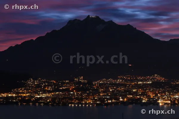 Silhouetten des Berges Pilatus vor einem violetten Abendhimmel über dem beleuchteten Luzern