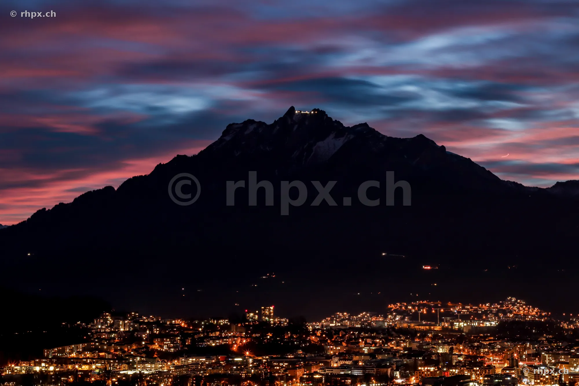 The dark Mount Pilatus with illuminated summit above the night lights of Lucerne
