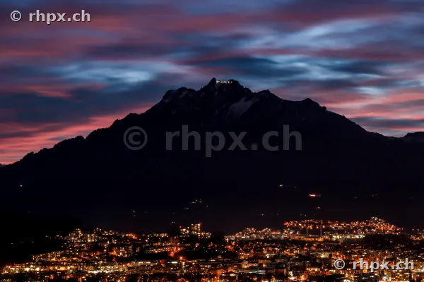 Der dunkle Pilatus mit beleuchtetem Gipfel über den nächtlichen Lichtern von Luzern