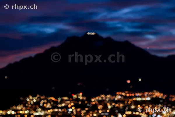 Unscharfe Lichter der Stadt vor der dunklen Silhouette des Pilatus in der Dämmerung