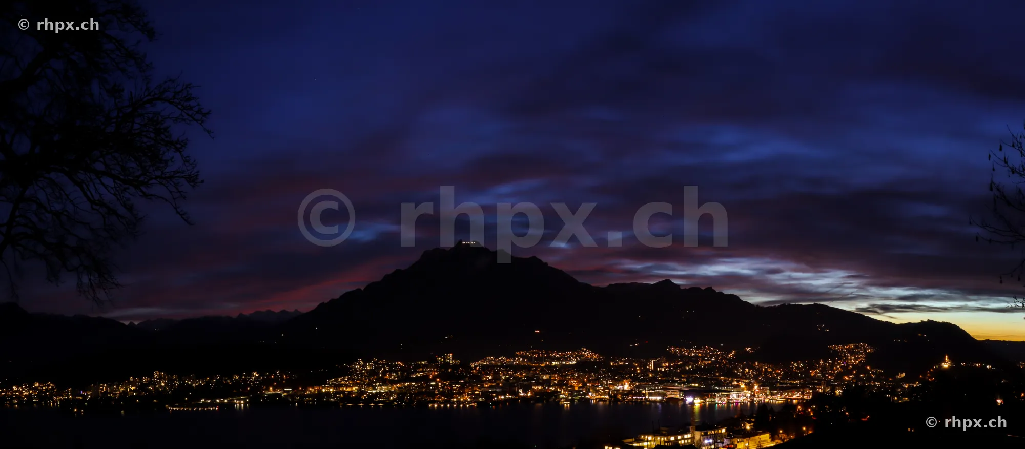Dark blue evening sky over Mount Pilatus and the lights of the city of Lucerne by Lake Lucerne.