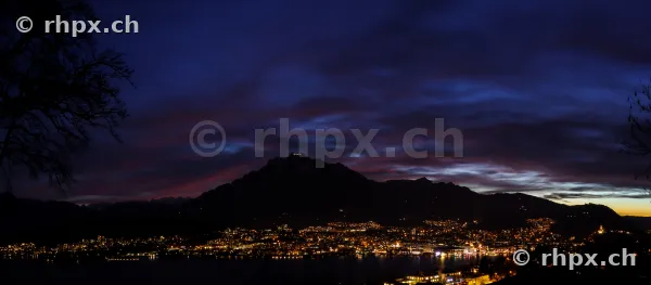 Dark blue evening sky over Mount Pilatus and the lights of the city of Lucerne by Lake Lucerne.