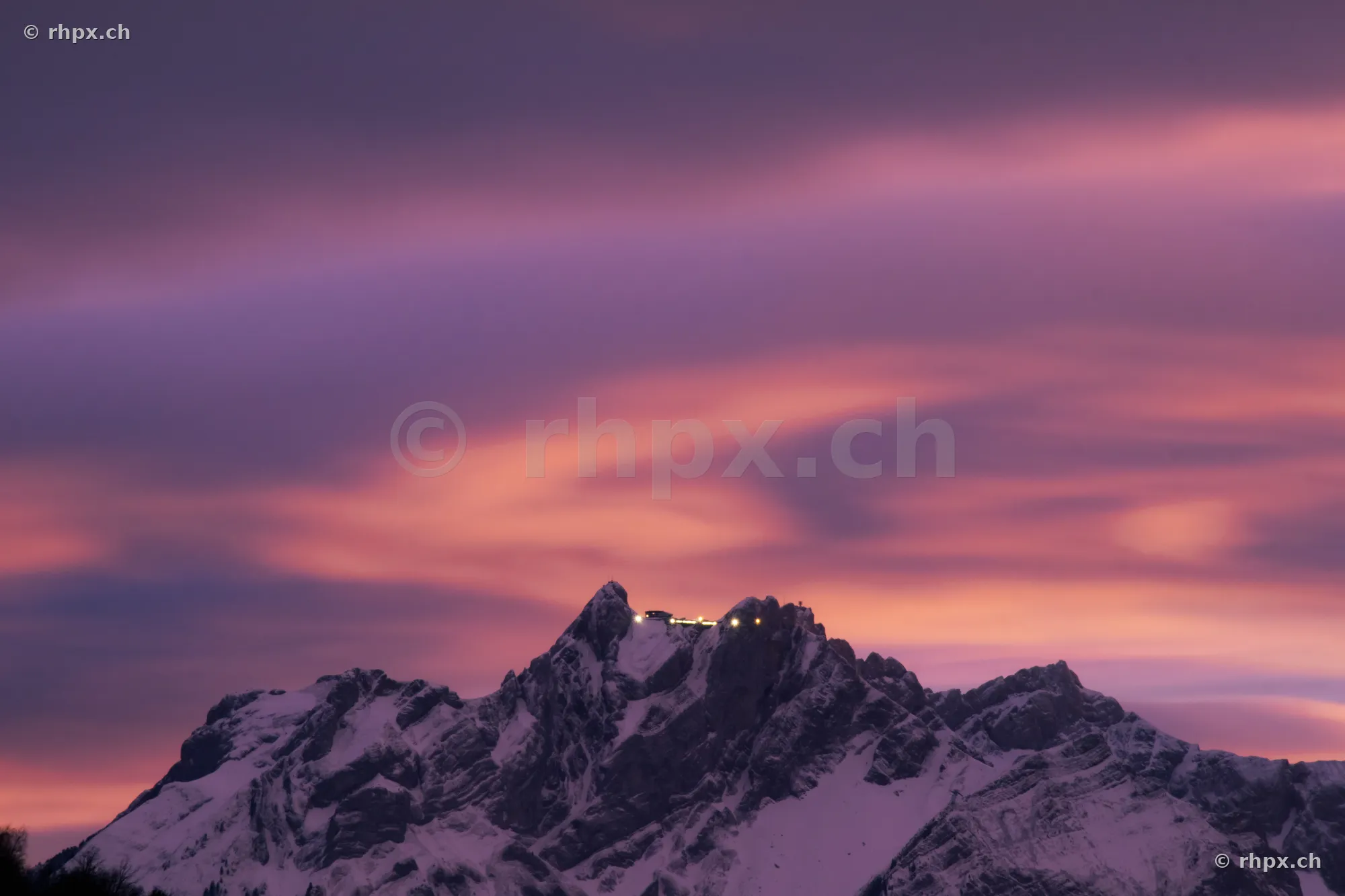 The snow-covered summit of Mount Pilatus at dusk with illuminated hotel