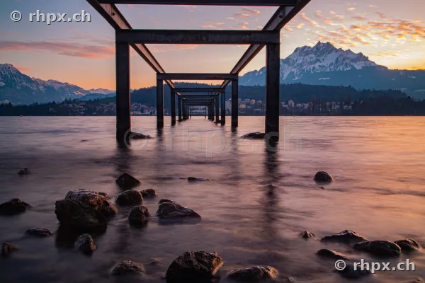 Blick durch einen Stahlsteg im Vierwaldstättersee auf den Pilatus bei Sonnenuntergang