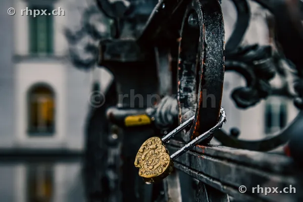 A golden love padlock attached to a dark metal railing with a blurred background in Lucerne