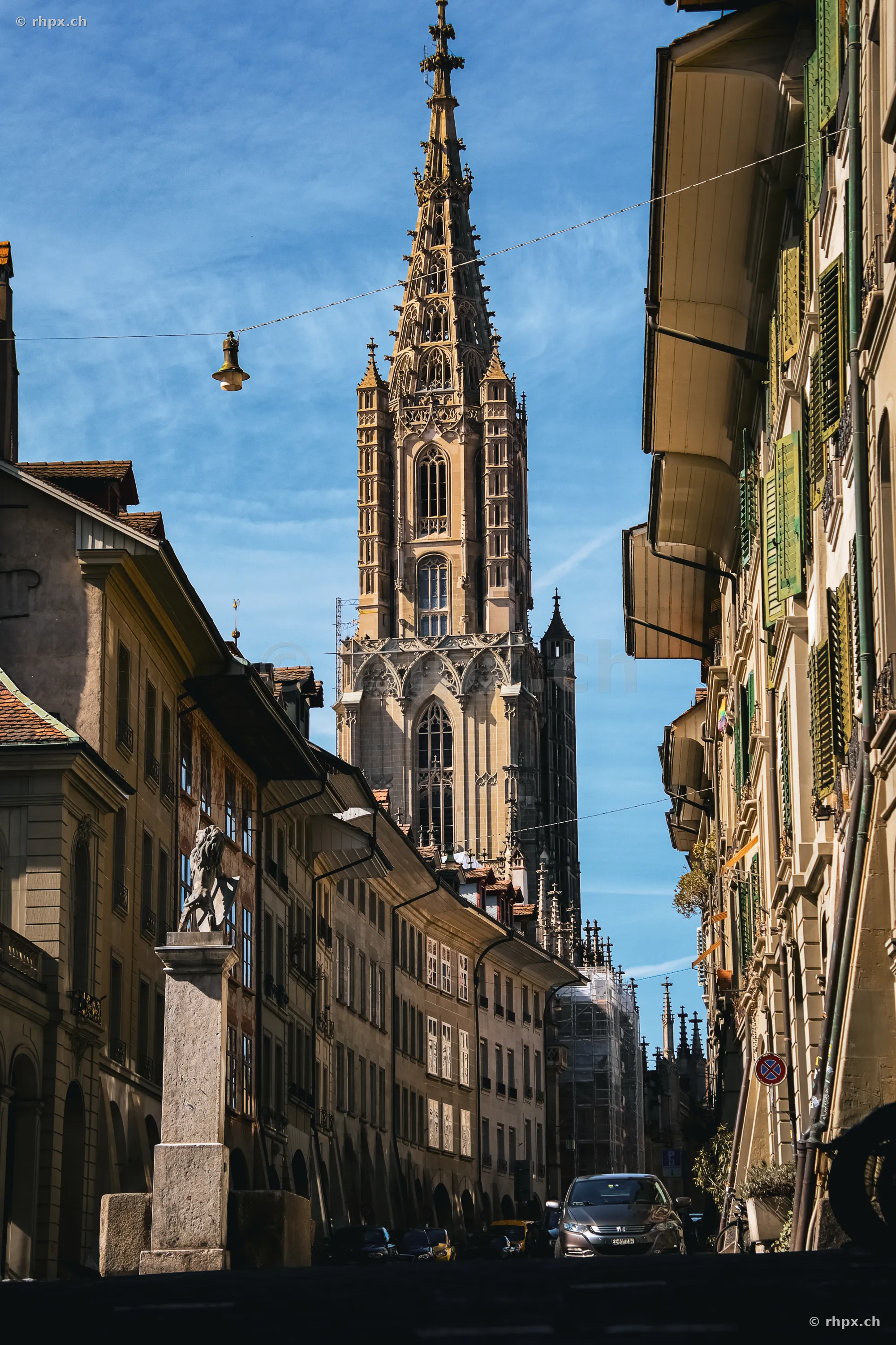 Blick durch eine Gasse der Berner Altstadt auf das Berner Münster bei klarem Himmel.