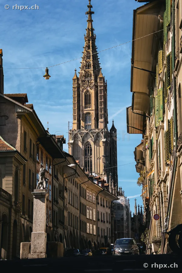 Blick durch eine Gasse der Berner Altstadt auf das Berner Münster bei klarem Himmel.