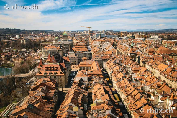 Blick von oben auf die roten Ziegeldächer der Berner Altstadt mit dem Bundeshaus im Hintergrund.