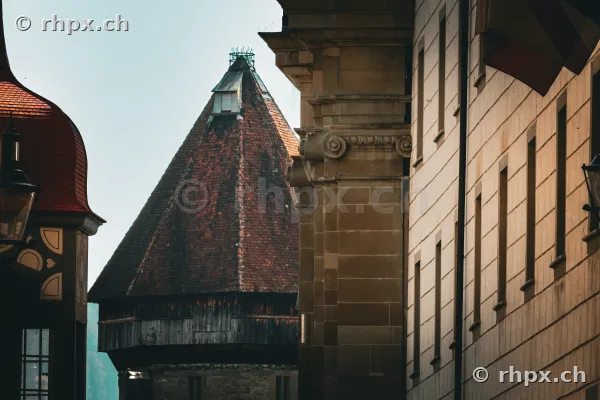 Blick auf den spitz zulaufenden Turm der Museggmauer in Luzern zwischen historischen Gebäudefassaden